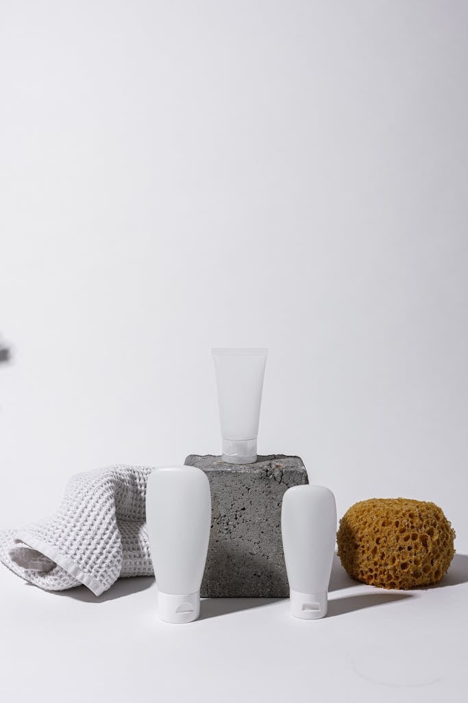 A clean and elegant spa setup with cosmetic bottles, sponge, and towel on a white background.
