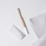 Aesthetic flat lay of wooden toothbrush, toothpaste tube, and cloth on white surface.