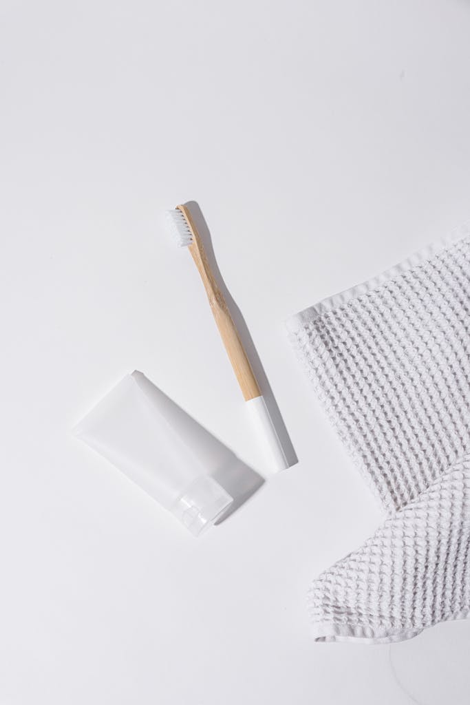Aesthetic flat lay of wooden toothbrush, toothpaste tube, and cloth on white surface.