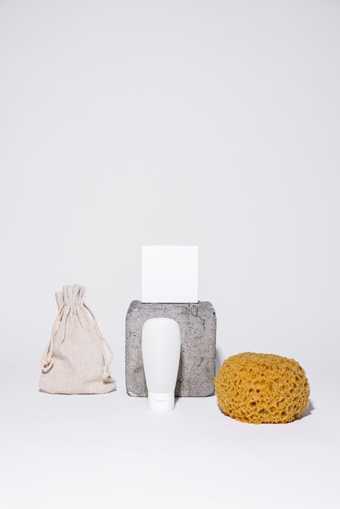 Minimalist setup featuring skincare items, sponge, and pouch on white background.