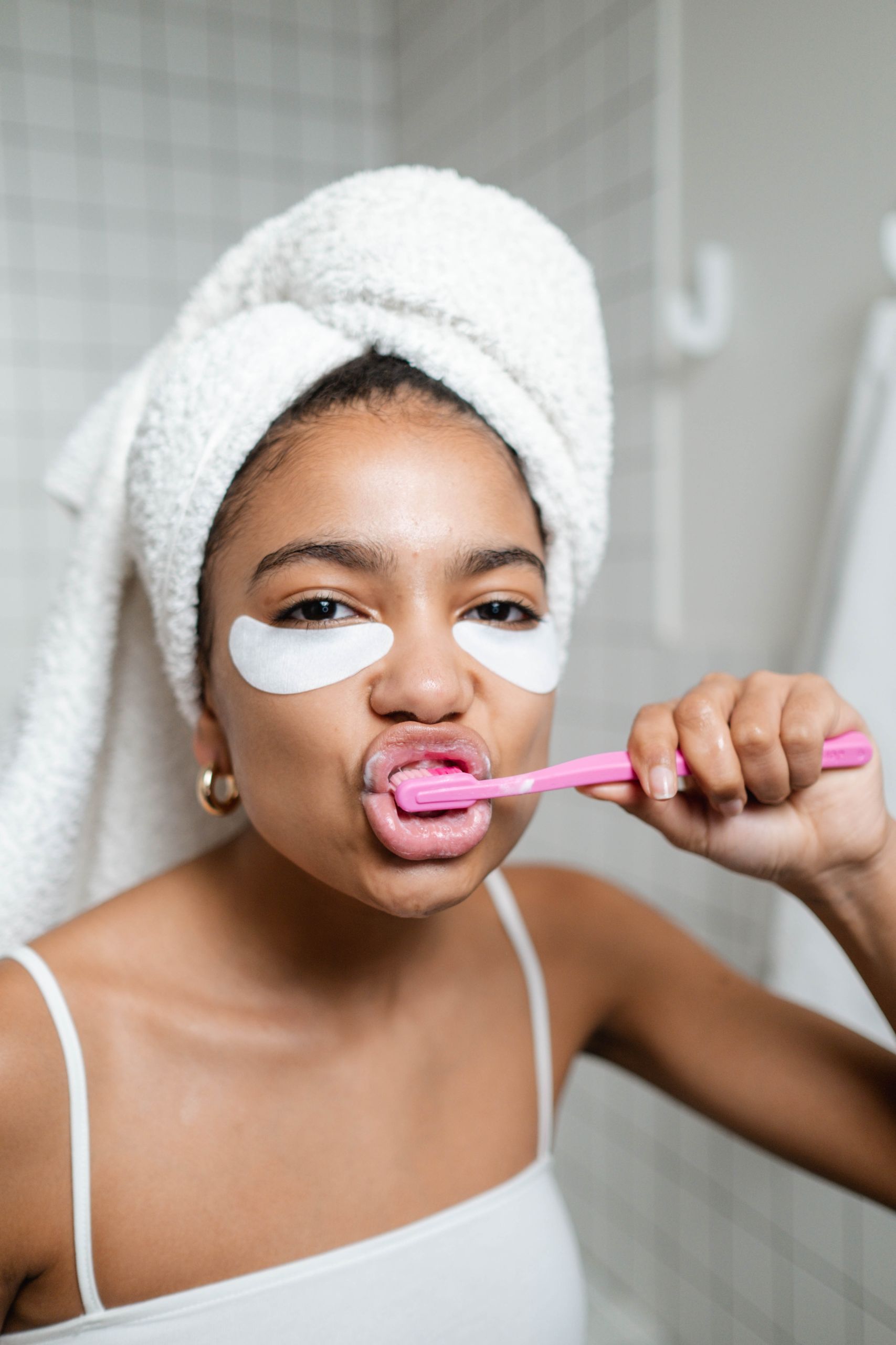 Accueil Adult woman brushing teeth with under-eye masks, showcasing personal care routine.