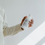 Elegant shot of a hand holding a white plastic bottle with shadows on a wall.