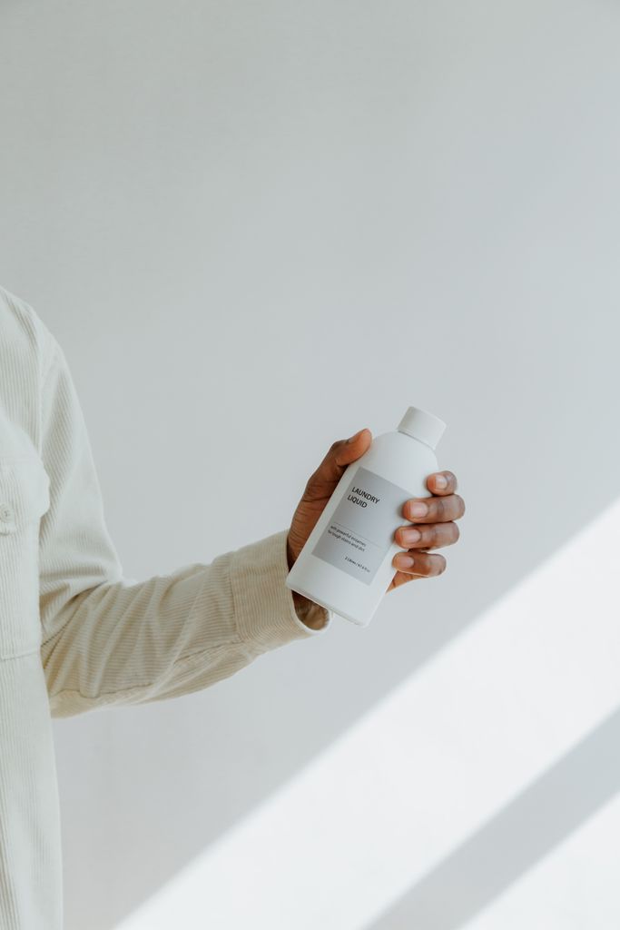 Elegant shot of a hand holding a white plastic bottle with shadows on a wall.