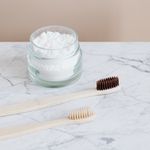 Zero waste concept reusable glass jar with organic toothpaste and wooden environmentally friendly toothbrushes placed on marble tabletop against beige wall