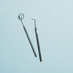Close-up of stainless steel dental tools on a pastel blue surface, ideal for healthcare themes.