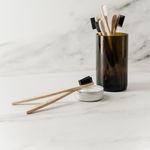Sustainable bamboo toothbrushes in a glass cup with tooth powder, promoting zero waste hygiene.