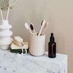 Collection of bamboo toothbrushes and organic natural soaps with wooden body brush arranged with recyclable glass bottle with natural oil and ceramic vase with artificial plant