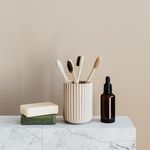 Sustainable consumption concept collection of assorted bamboo toothbrushes and natural soaps near reusable dark glass bottle with oil on marble table against plain beige wall