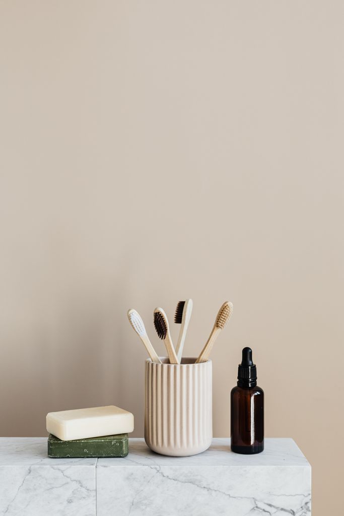 Sustainable consumption concept collection of assorted bamboo toothbrushes and natural soaps near reusable dark glass bottle with oil on marble table against plain beige wall